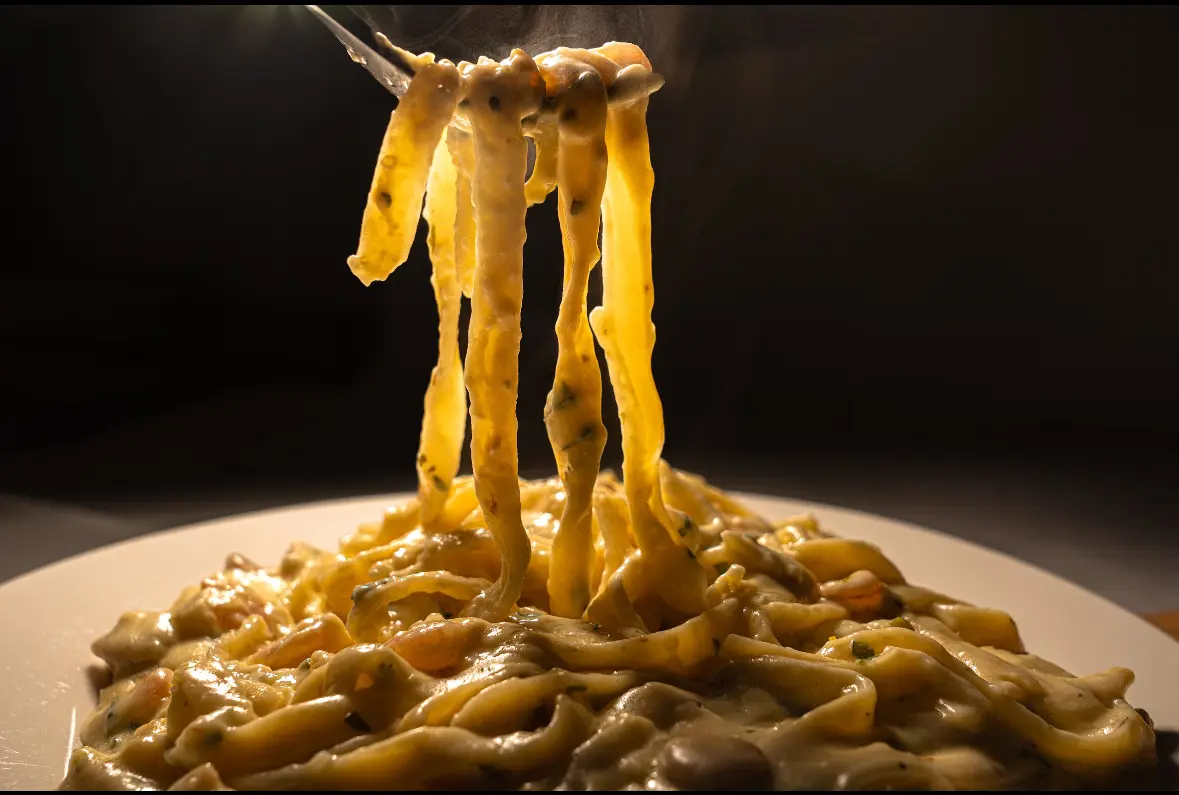 Fork lifting creamy pasta in dark background.